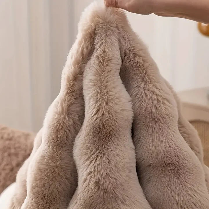 Close-up of a hand holding up a luxuriously soft beige long-pile faux fur pet blanket showing deep plush texture in a cozy home setting