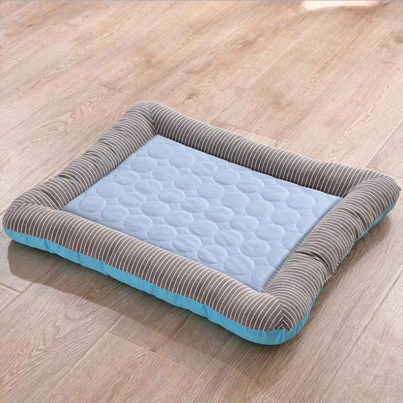 A rectangular pet cooling mat with a light blue quilted center and a striped gray fabric border, shown on a light wood floor.