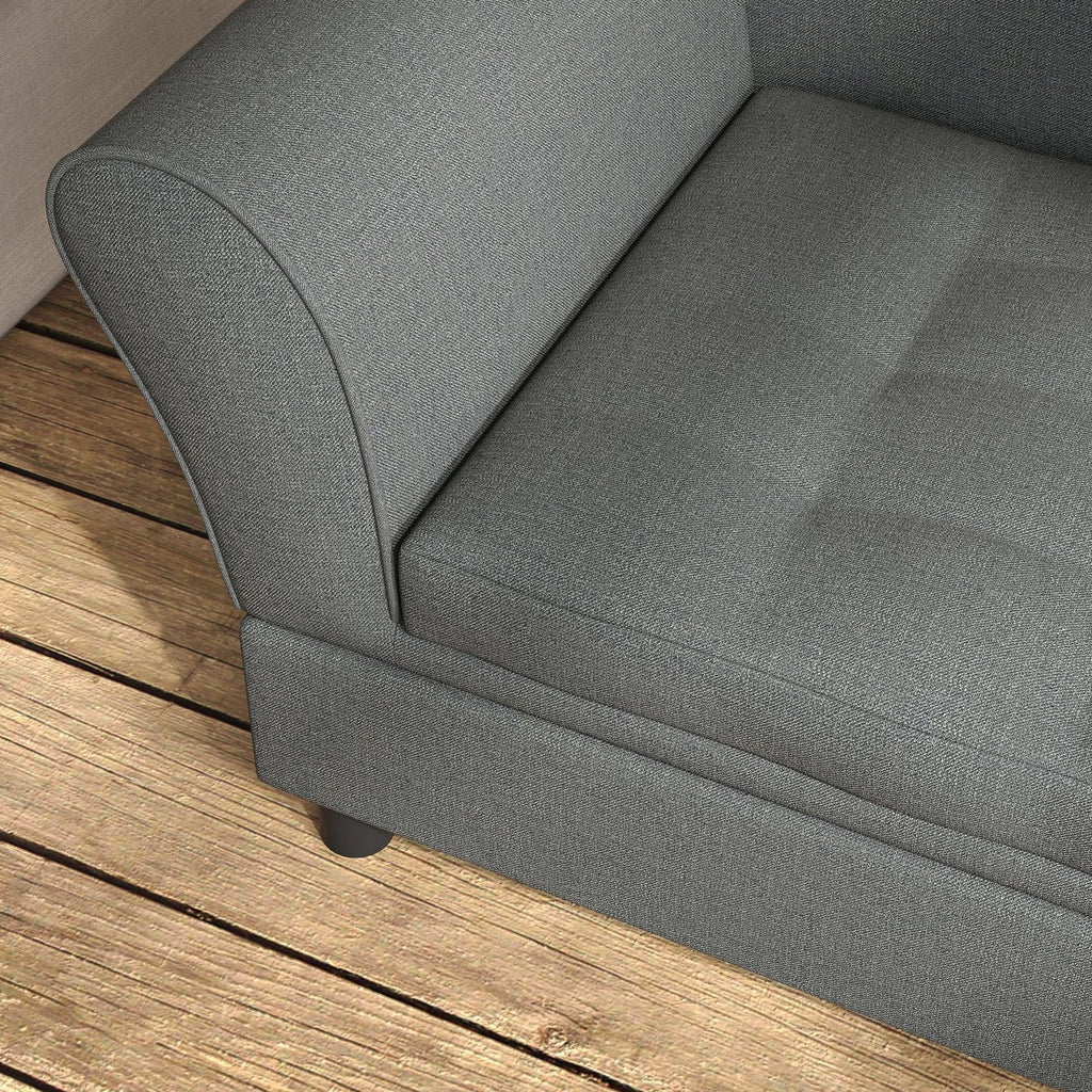 Close-up of a gray upholstered sofa corner with a tufted seat cushion and dark legs, shown on a wooden deck floor.