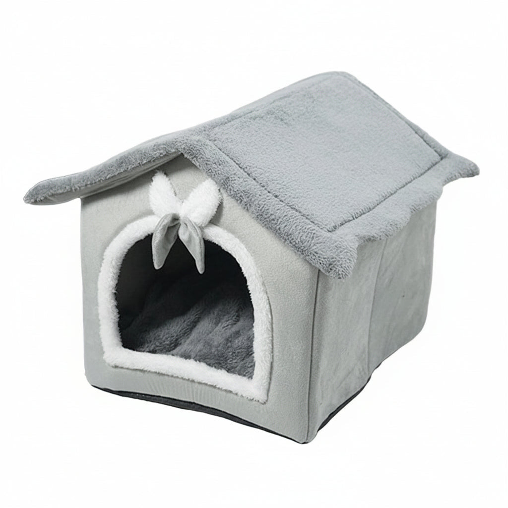 A gray plush pet house with a slanted roof, arched entryway, white faux-fur trim, and a small white bow on the front, shown on a plain white background.