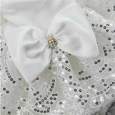 Close-up of a white pet dress with sequined floral lace and a satin bow with a rhinestone center