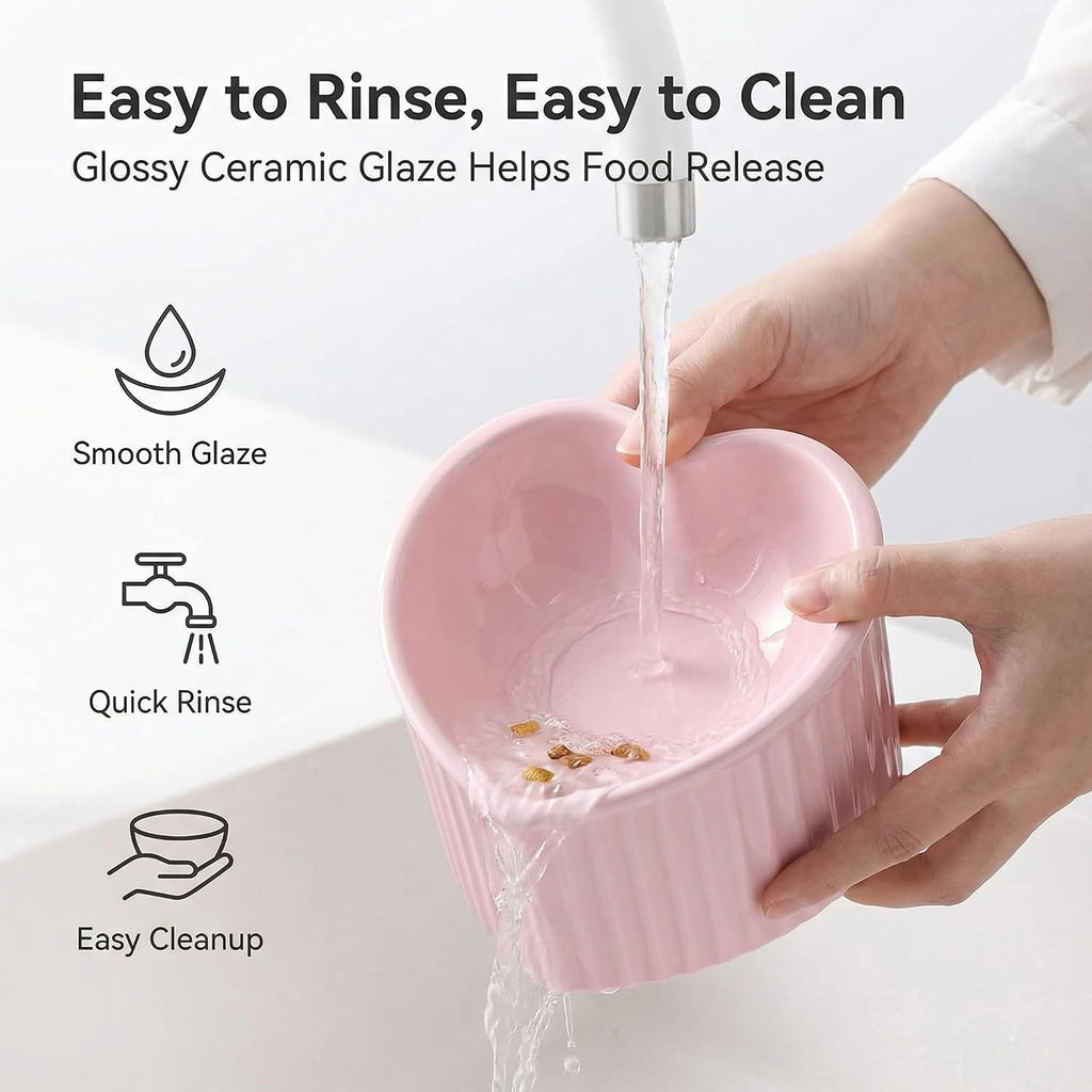 Infographic showing hands rinsing a pink ceramic heart-shaped pet bowl under running water with text highlighting smooth glaze, quick rinse, and easy cleanup features, white background

