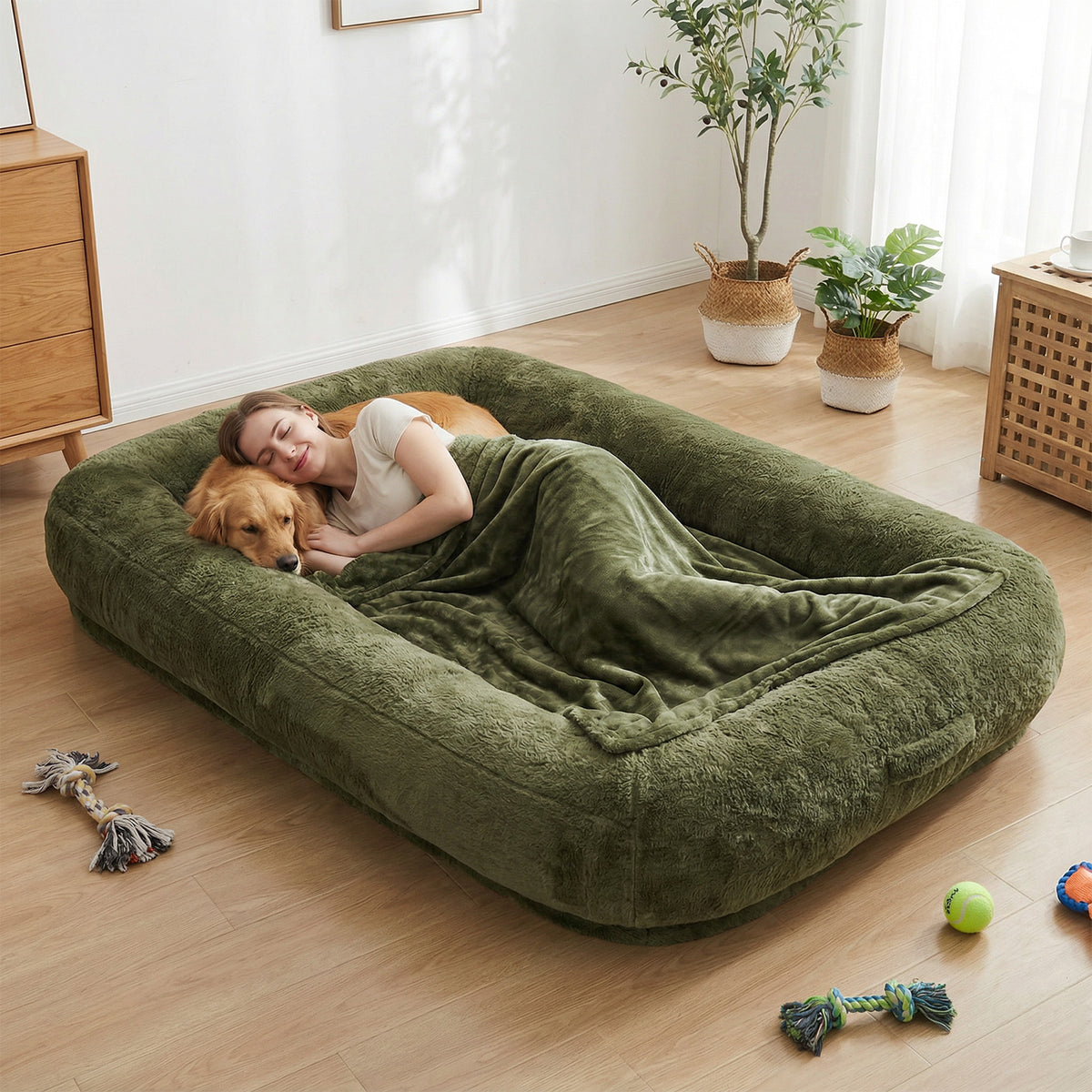 Woman and Golden Retriever cuddling together on an oversized olive green plush human-sized dog bed with bolster sides and matching blanket in a modern living room