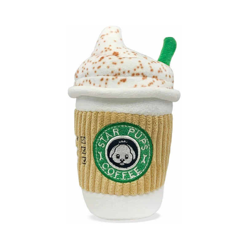 A plush toy shaped like a Starbucks coffee cup, featuring a cream-colored whipped foam top with brown speckles, a green straw, a beige ribbed sleeve, and a green Starbucks logo patch on the front.