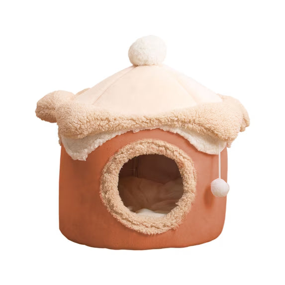 A small plush pet house with a rounded terracotta-orange body, cream sherpa trim, and a cream dome roof with a pom-pom on top, shown on a plain white background.