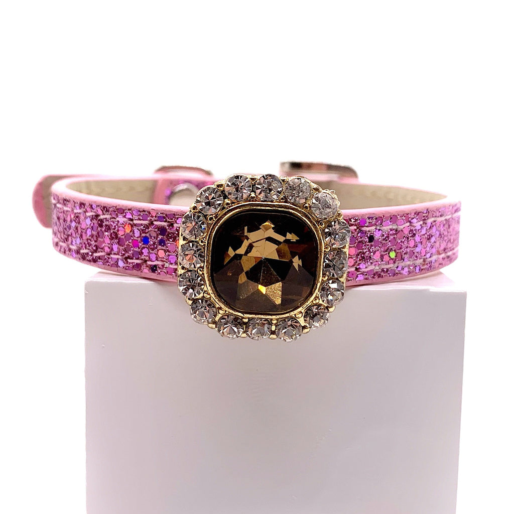 A pink rhinestone-embellished collar with a central gold-tone oval medallion and a halo of clear crystals, displayed on a white block against a white background.