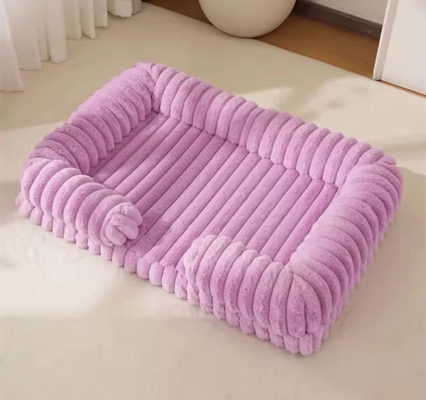 Lavender chunky corduroy pet bed on a cream floor in a minimal, light-filled room with a white sphere ornament in the background.