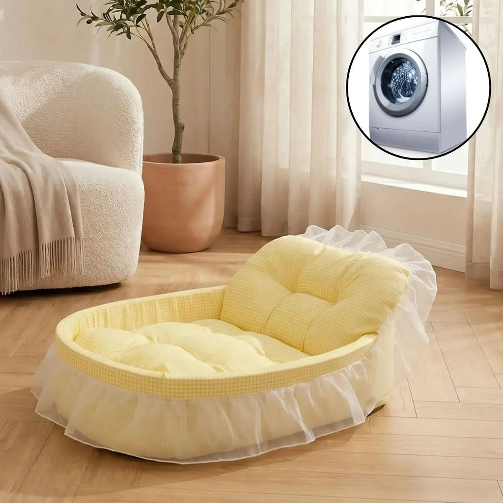 A pastel yellow tufted pet bed with a white tulle ruffle base, shown in a bright living room. A circular inset in the top right shows a washing machine, suggesting a laundry or laundry-drying use case.