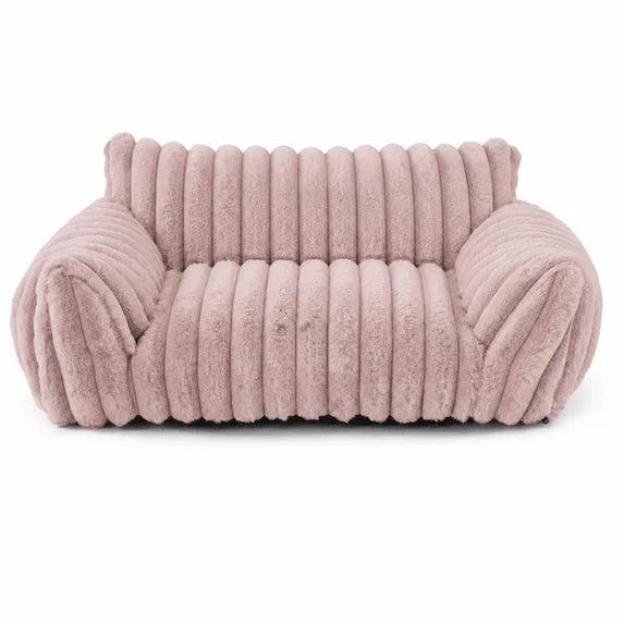 Blush pink rectangular pet sofa bed with thick ribbed channel-tufted plush fabric, rounded raised back and armrests, and a deep cushioned seat, shown from the front on a white background