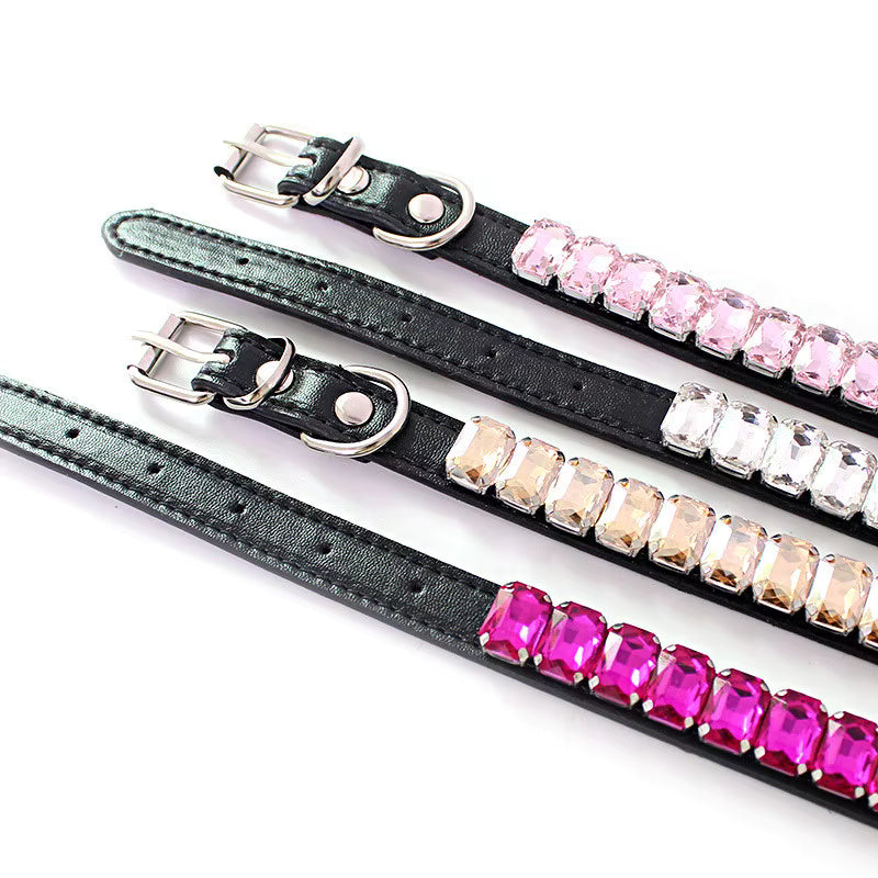 Close-up of several black pet collars with silver buckles and rows of pale pink, clear, cream, and hot-pink rectangular rhinestones on a white background.