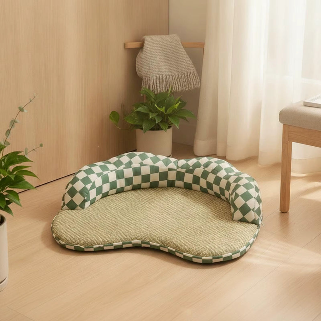 A pet bed with a green and white checkered bolster and a textured beige cushion, placed on a light wood floor in a bright, modern room.