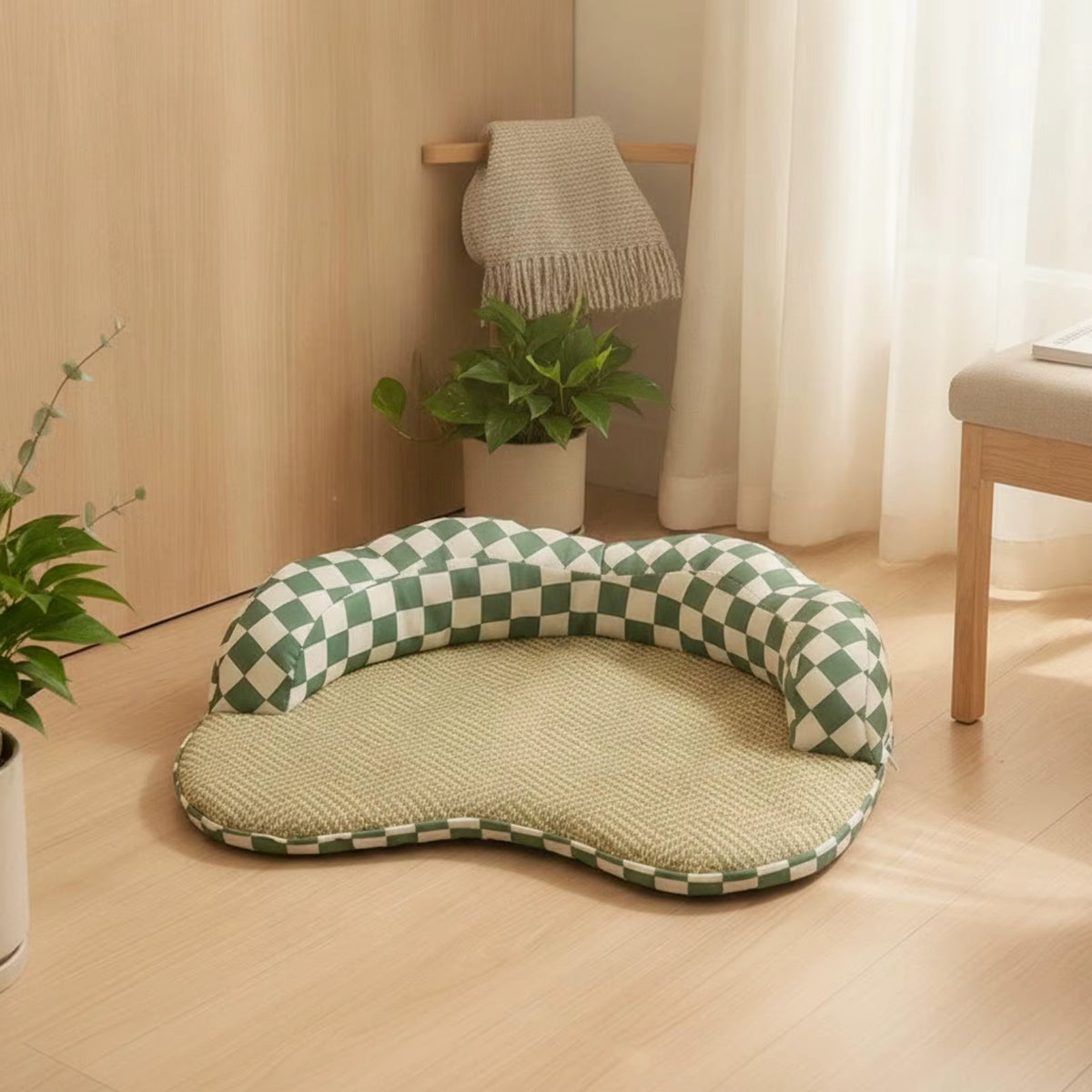 A pet bed with a green and white checkered bolster and a textured beige cushion, placed on a light wood floor in a bright, modern room.