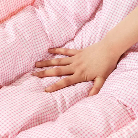 Close-up of a hand pressing into the plush tufted cushion of a pink gingham pet bed, demonstrating soft memory foam filling