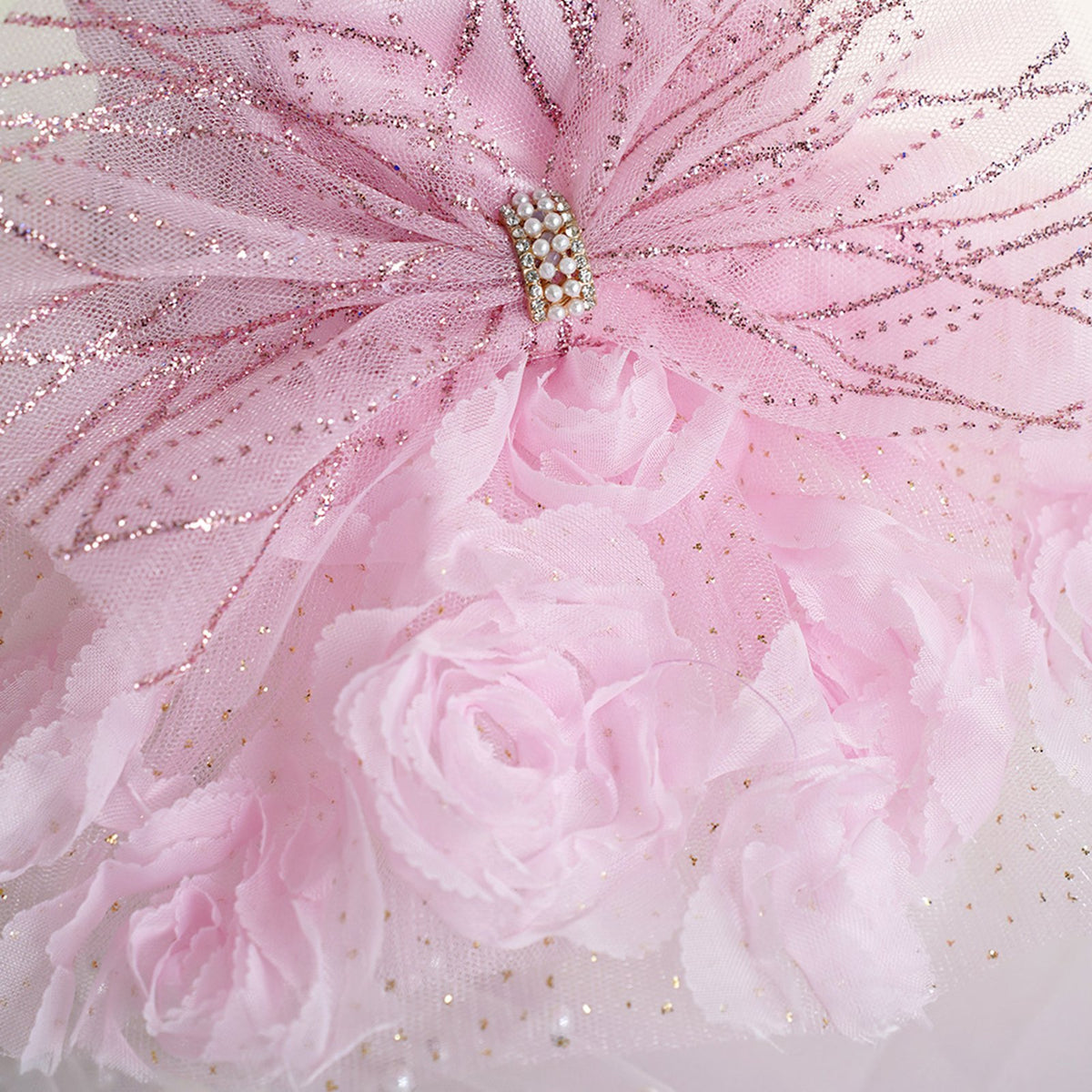 Close-up of a pink pet dress with a glitter-patterned tulle bow, pearl and rhinestone center, and pink fabric roses