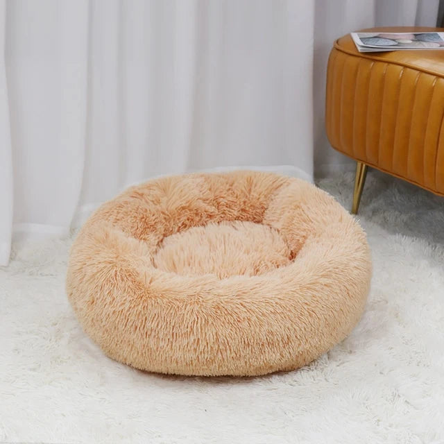 Fluffy beige pet bed on a white carpet with a blurred background