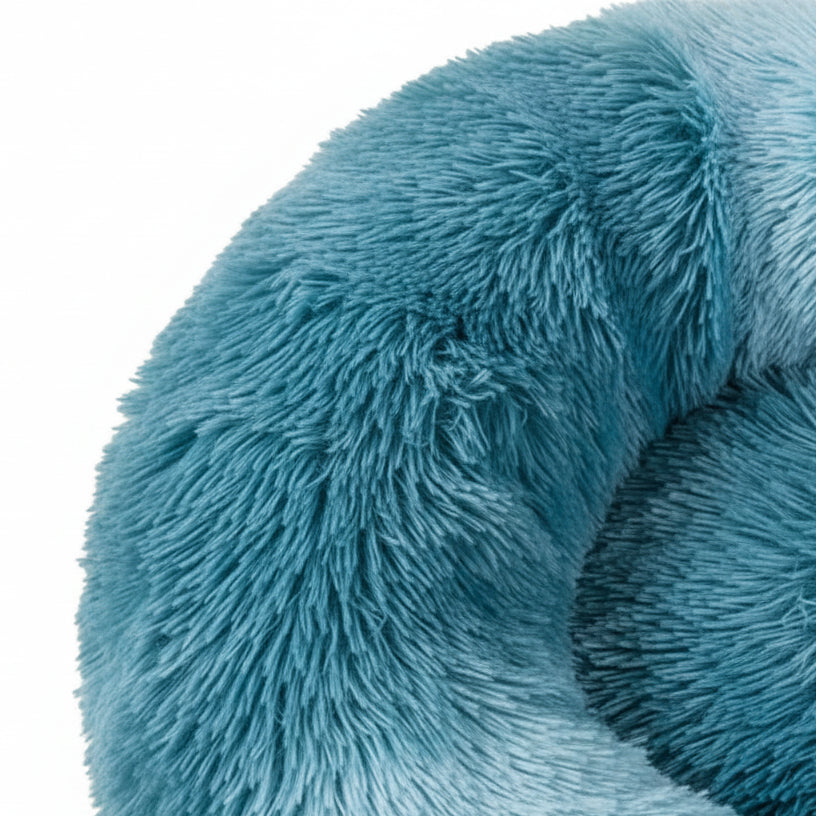 Close-up texture detail of round teal shaggy faux fur donut calming pet bed showing plush long-pile fur material on white background