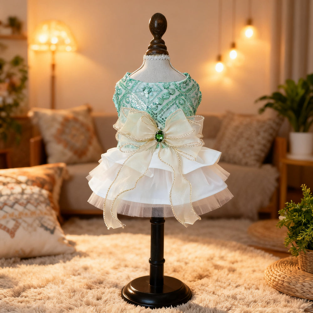 Mint green sequined dog dress on a mannequin with a white tiered ruffle skirt and gold-trimmed ivory bow with a green jewel centerpiece
