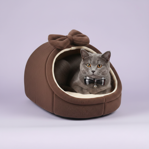 Grey British Shorthair cat with plaid bow tie and bell collar resting inside a rich brown plush igloo cat cave bed with matching bow detail and cream fleece interior, lavender background