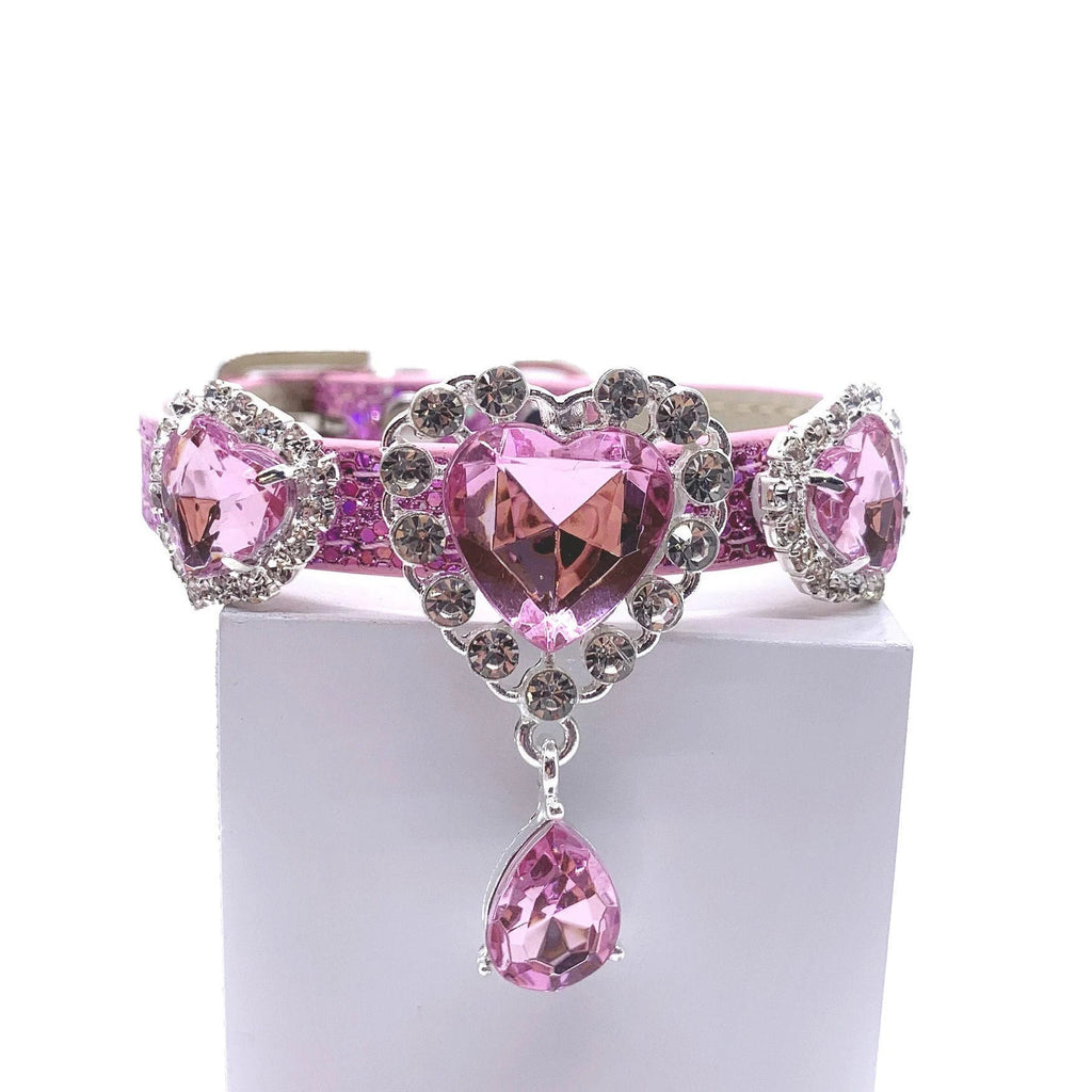Pink glitter pet collar with three rose pink heart crystal charms in rhinestone halo settings, center charm with dangling pink teardrop crystal drop, laid flat showing full length with rhinestone-encrusted buckle for cats and dogs