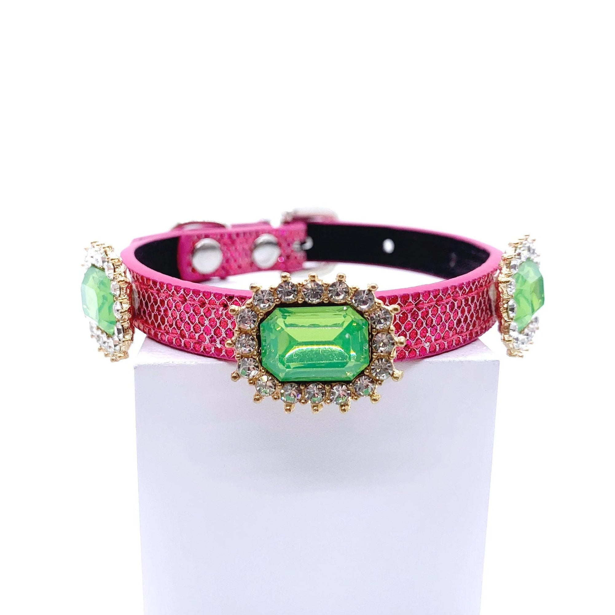 Hot pink metallic honeycomb texture pet collar with three peridot green emerald-cut crystal charms in gold rhinestone sunburst halo settings displayed on stand for cats and dogs