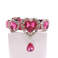 Hot pink metallic glitter pet collar with three fuchsia heart crystal charms in rhinestone halo settings, center charm with dangling pink teardrop crystal drop, displayed on stand for cats and dogs