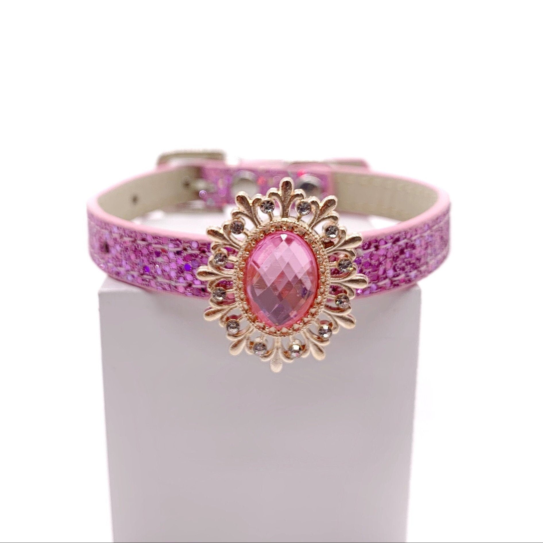 Pink glitter pet collar with gold ornate sunburst brooch and rose pink faceted oval crystal centerpiece with rhinestone accents displayed on stand for cats and dogs