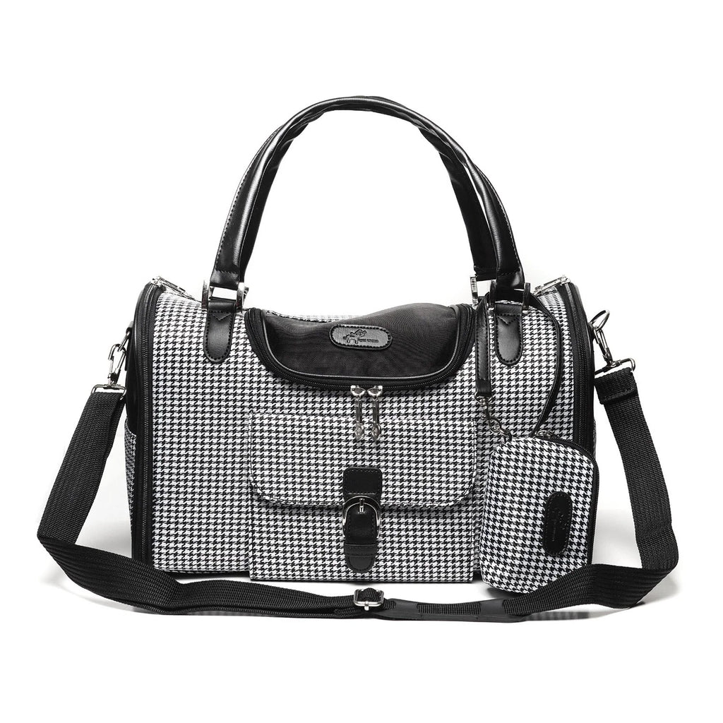 A black and white houndstooth pattern  pet carrier with black leather trim, dual top handles, a front flap pocket, and an adjustable shoulder strap, shown on a plain white background.