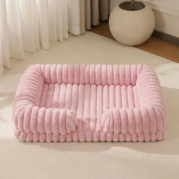 Blush pink chunky corduroy pet bed with a low front entry, photographed from the front on a cream floor in a minimal, light-filled room with sheer curtains and a white sphere ornament.