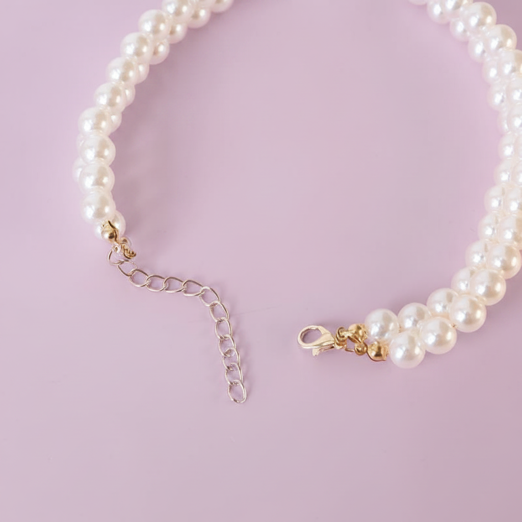 Close-up detail shot of the double-strand white pearl pet collar showing the gold lobster clasp closure and adjustable gold extension chain, laid flat in a circular shape on a soft lavender background