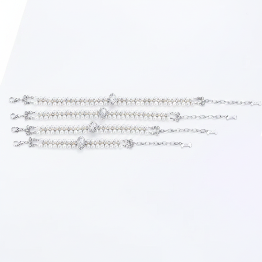 Four double-strand white pearl pet collars laid flat in a row, each with silver hardware, crystal accents between the pearls, and a marquise-cut clear crystal centerpiece — shown in graduating sizes (XS through L) on a white background
