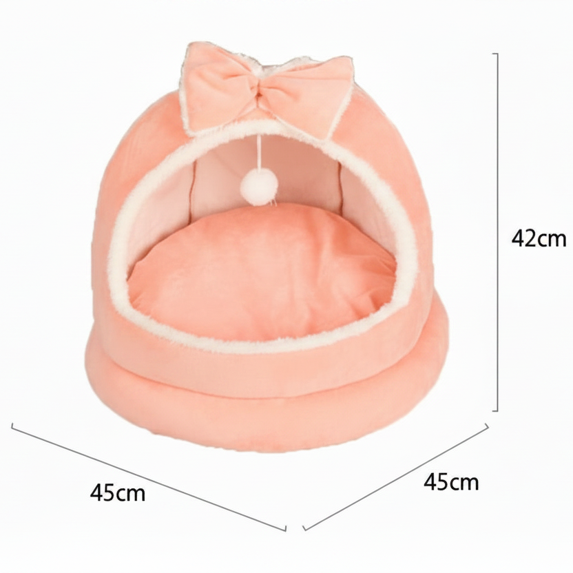 Pink plush dome cat bed with bow on top and hanging white pom pom ball showing dimensions — 45cm wide by 45cm deep by 42cm tall — on a white background