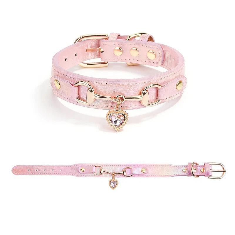 Pink leather pet collar with rose gold snaffle-bit hardware and clear crystal heart charm pendant, shown in close-up and full-length views on a white background
