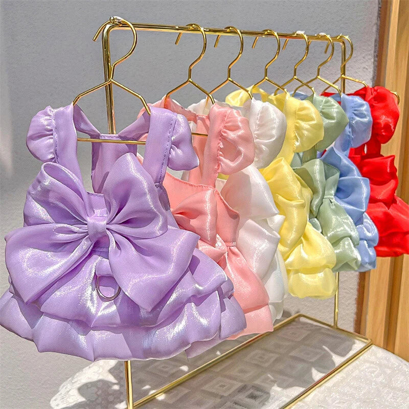 Satin pet dresses with puff sleeves, ruffled skirts, and oversized bows in lavender, pink, white, yellow, mint green, blue, and red