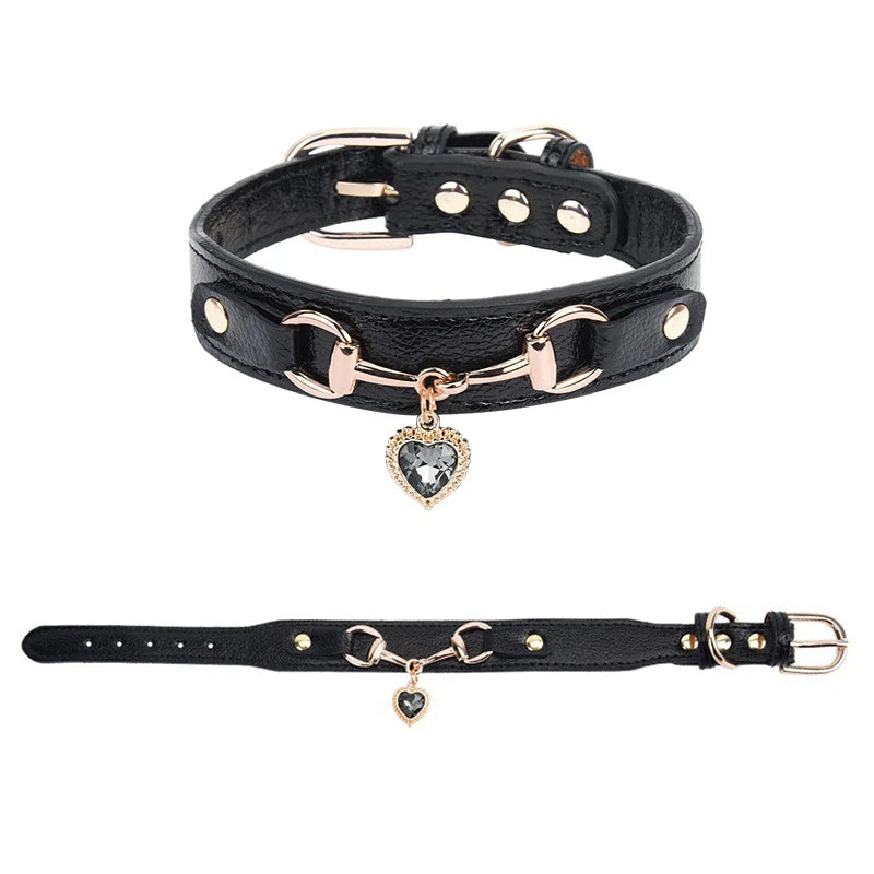 Black leather pet collar with rose gold snaffle-bit hardware and grey crystal heart charm pendant, shown in close-up and full-length views on a white background