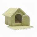 Sage green textured ribbed plush house-shaped pet bed with white scalloped roof trim, small multicolor flower accent above the arched entrance, detachable side door panel, and beige cushioned floor mat with blue ruffle trim shown unfolded open, on a white background