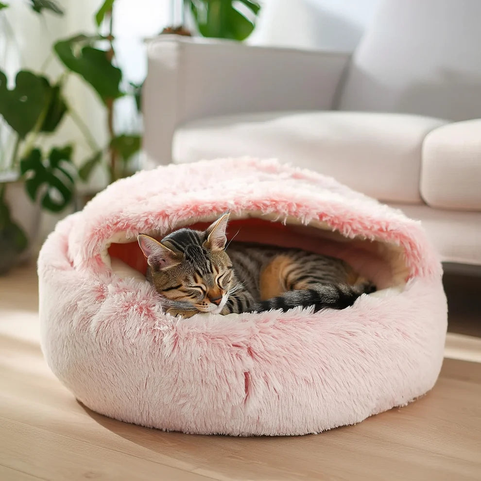 Tabby cat sleeping inside a blush pink long-pile plush round hooded cave pet bed in a cozy living room setting