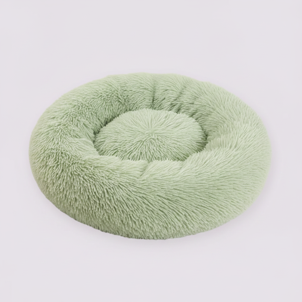 Sage green round donut pet bed with long shaggy faux fur and a plush cushioned center, shown against a soft lavender background