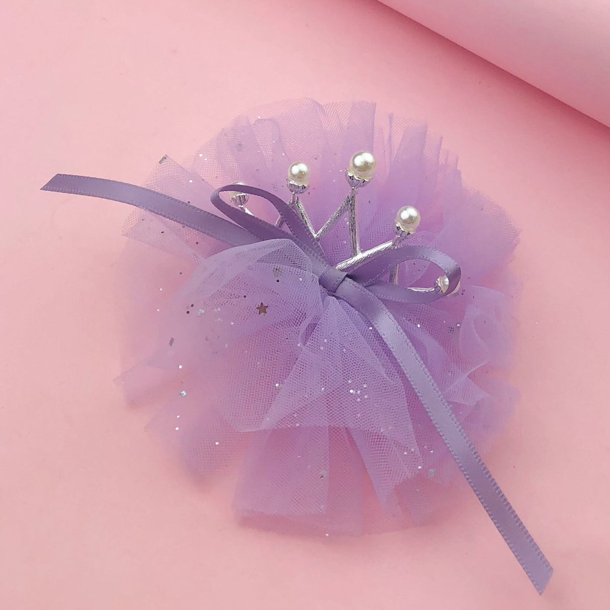 Lavender tulle pet crown with pearl-tipped silver points, glitter star accents, and purple satin ribbon ties on a pink background